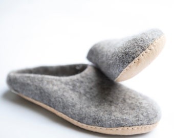 May include: A pair of gray felt slippers with a tan leather trim. The slippers are folded over, showing the inside of the slipper.