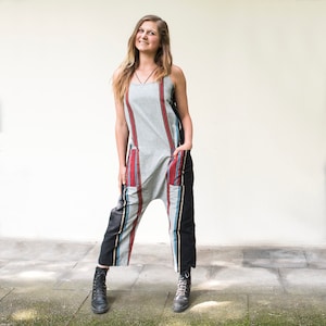 Può includere: Una donna indossa una tuta a righe grigie e nere con accenti rossi e blu. La tuta ha una vestibilità ampia e presenta tasche sul davanti. Indossa stivali neri.