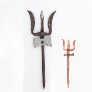 May include: Two trident-shaped objects on a white background. The larger trident is made of dark metal with a silver axe-like piece attached. The smaller trident is copper-coloured.