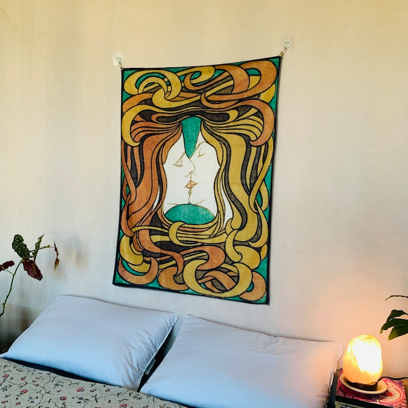 Peter Behrens The Kiss tapestry displayed vertically above a bed, showing the full green, yellow, orange and black Art Nouveau design.