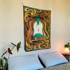 Art Nouveau The Kiss tapestry hanging above a bed, with intertwined faces, flowing yellow and orange forms, green background and black outlines.