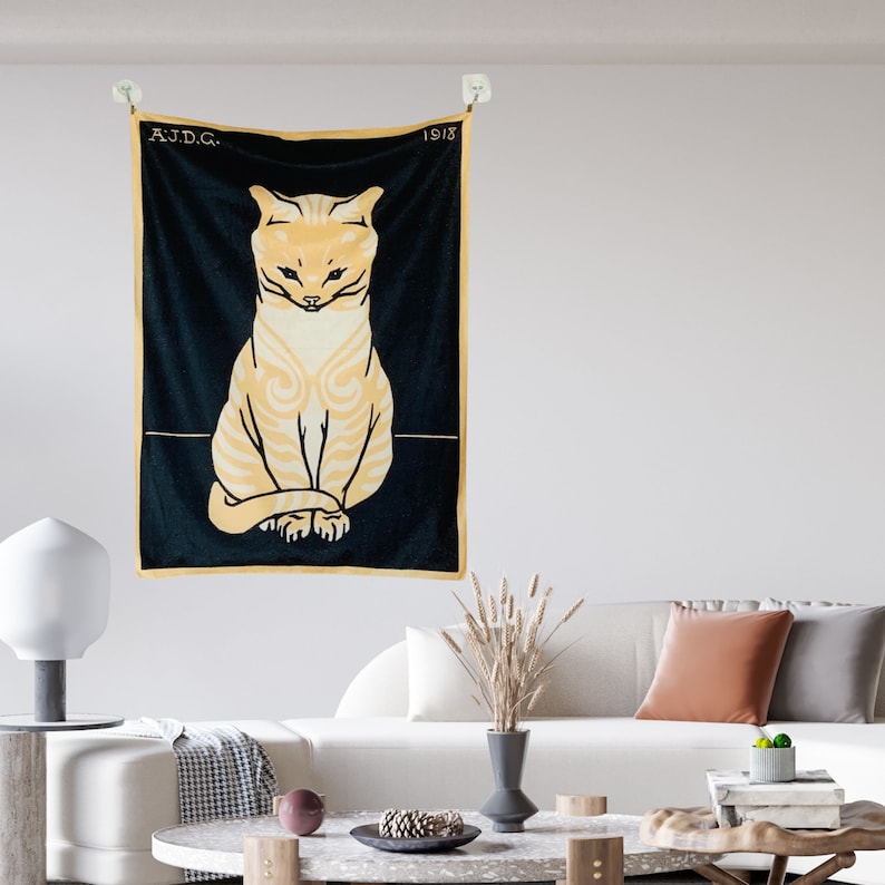 A Julie de Graag cat print tapestry hanging above a modern white living room sofa styled with rust and grey accent pillows. The vintage graphic animal wall art adds a striking contrast to the bright contemporary space.