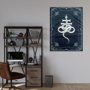 Op de afbeelding: Een zwart-witte wandkleed met een witte slang die om een kruis is gewikkeld op een donkerblauwe achtergrond. Het wandkleed heeft een decoratieve rand met een geometrisch patroon.