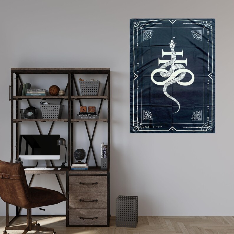 Op de afbeelding: Een zwart-witte wandkleed met een witte slang die om een kruis is gewikkeld op een donkerblauwe achtergrond. Het wandkleed heeft een decoratieve rand met een geometrisch patroon.