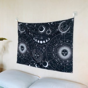 Angled view of black and white astrology tapestry above a bed, showing zodiac wheels, moon phases, constellations, and celestial faces.