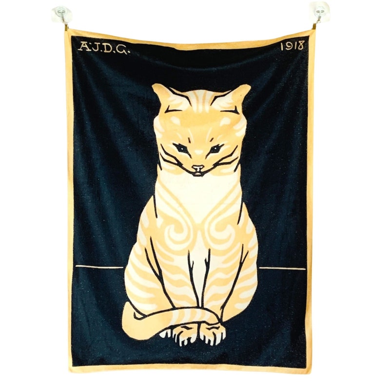 Full flat product view of the vintage Dutch cat wall hanging suspended by silver clips against a white background. The tapestry features Julie de Graag's bold 1918 illustration of a cream and yellow cat on a solid black background.