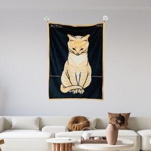 A Julie de Graag cat print tapestry hanging above a modern white living room sofa styled with rust and grey accent pillows. The vintage graphic animal wall art adds a striking contrast to the bright contemporary space.