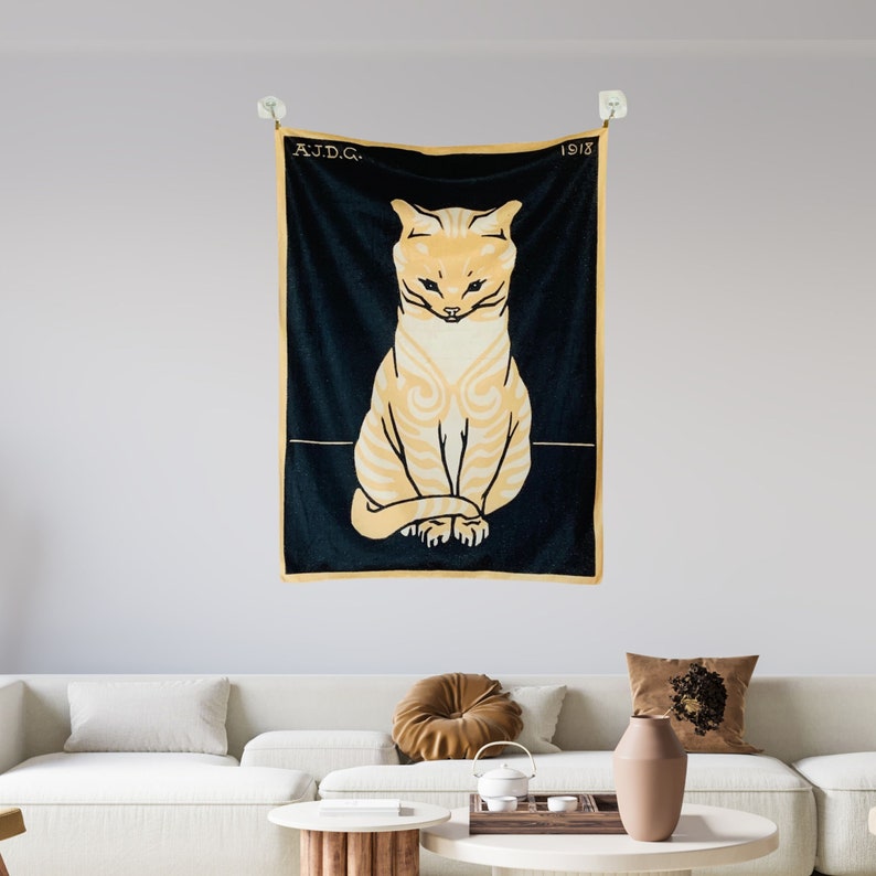 A Julie de Graag cat print tapestry hanging above a modern white living room sofa styled with rust and grey accent pillows. The vintage graphic animal wall art adds a striking contrast to the bright contemporary space.