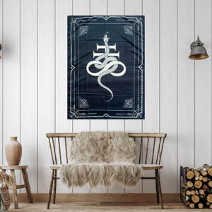 Op de afbeelding: Een zwart-wit tapijt met een witte slang die om een kruis is gewikkeld. Het tapijt is omlijst met een witte rand en ingewikkelde ontwerpen.