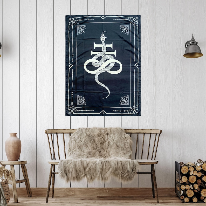 Op de afbeelding: Een zwart-wit tapijt met een witte slang die om een kruis is gewikkeld. Het tapijt is omlijst met een witte rand en ingewikkelde ontwerpen.