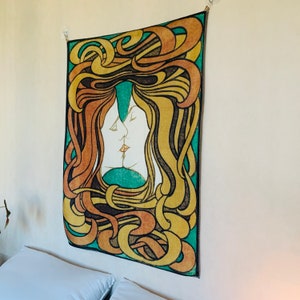 Side angle of The Kiss tapestry hanging above a bed, highlighting the lightweight fabric and flowing Jugendstil pattern.