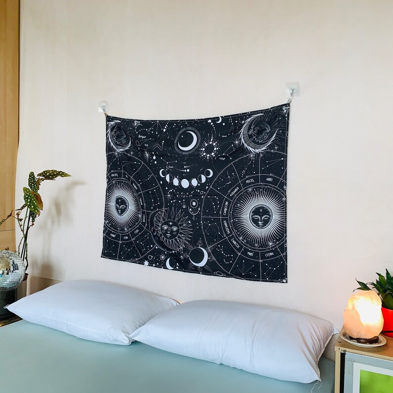 Angled bedroom view of black and white celestial zodiac tapestry, featuring moon phases, constellation patterns, and mystical sun moon imagery.