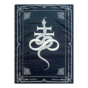 Op de afbeelding: Een zwart wandkleed met een witte slang die om een kruis is gewikkeld. Het wandkleed heeft een decoratieve rand.