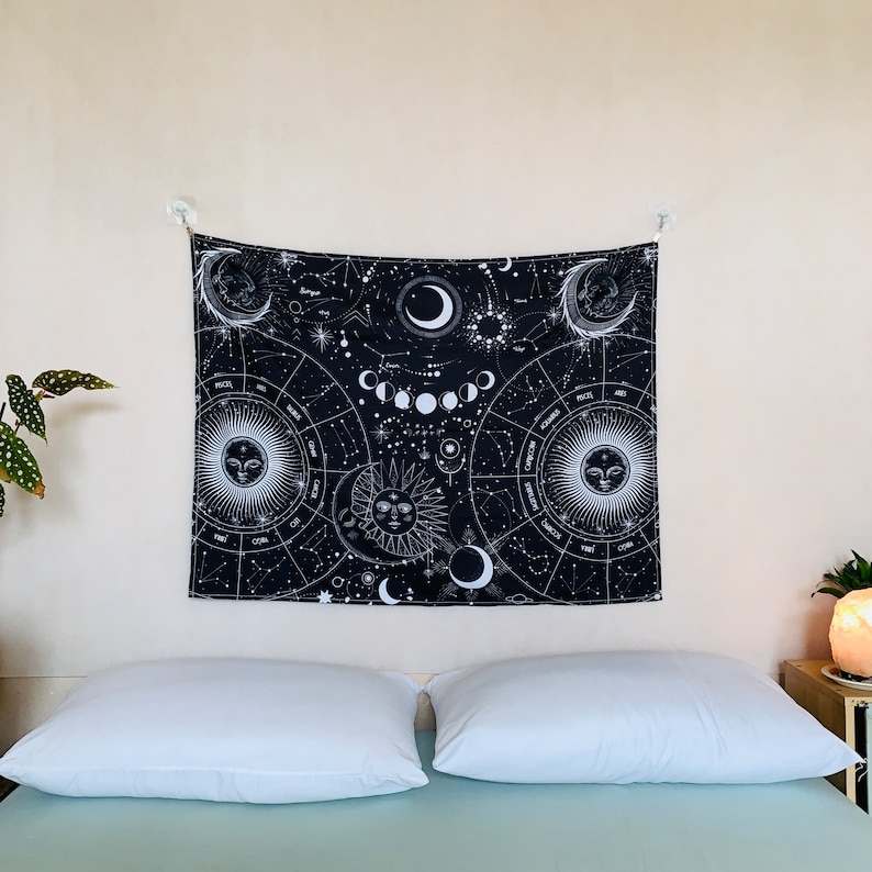 Wide room view of black and white zodiac tapestry above a bed, featuring moon phases, constellations, and celestial sun moon design.