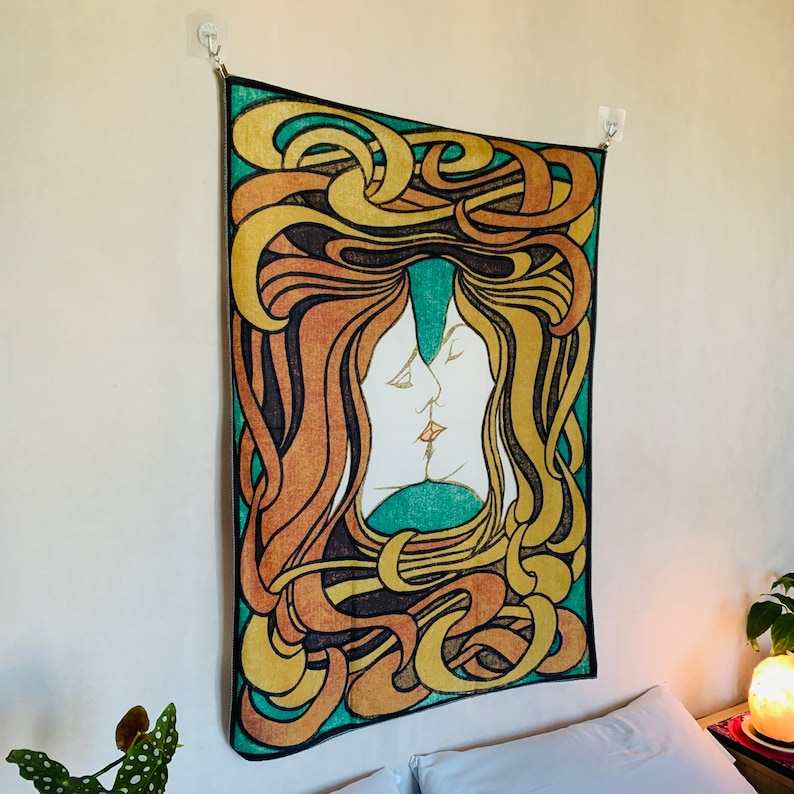 Angled close view of The Kiss tapestry above a bed, showing two intertwined profiles surrounded by sweeping Jugendstil curves.