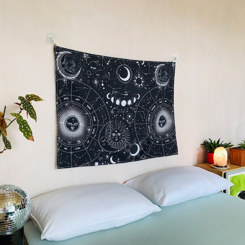 Angled bedroom view of black and white celestial zodiac tapestry, featuring moon phases, constellation patterns, and mystical sun moon imagery.