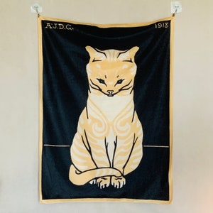 Straight-on, close-up view of the Julie de Graag Sitting Cat tapestry hanging flat against a light-colored wall using clear adhesive clips. The vintage Dutch animal wall hanging features a striking cream and yellow graphic illustration of a seated cat centered on a solid deep black background.