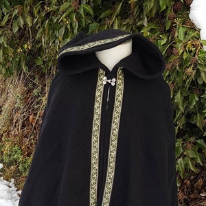 May include: A black hooded cloak with a green and gold trim. The cloak is worn over a green and white dress.