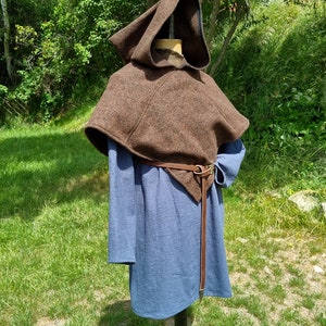 May include: A brown hooded cloak with a leather belt. The cloak is made of a thick, woven fabric and has a simple, functional design.
