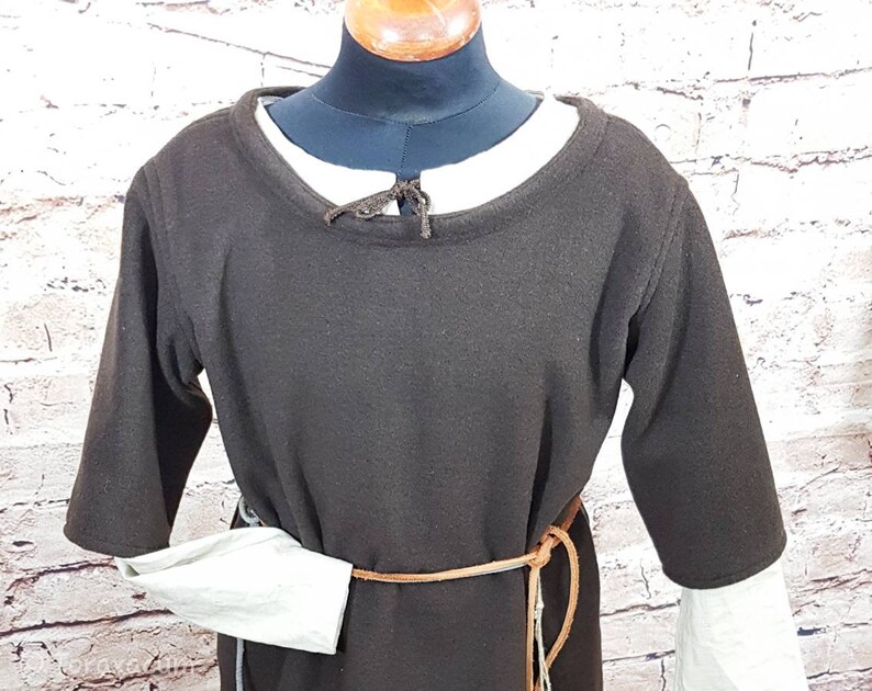 May include: A brown tunic with long sleeves and a round neckline. The tunic has a brown leather belt with a long strap hanging down the front. The sleeves are gathered at the wrists and have a white underlayer.
