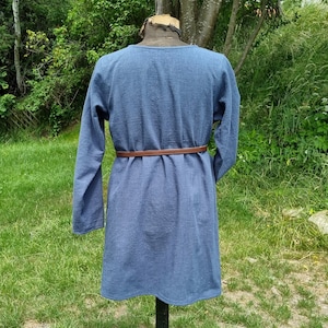 May include: A long-sleeved, blue tunic with a brown belt. The tunic is made of a textured fabric and has a simple, classic design.