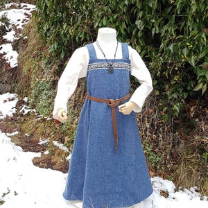 May include: A long, blue wool dress with a white linen underdress. The dress has a brown leather belt and a decorative trim around the neckline.