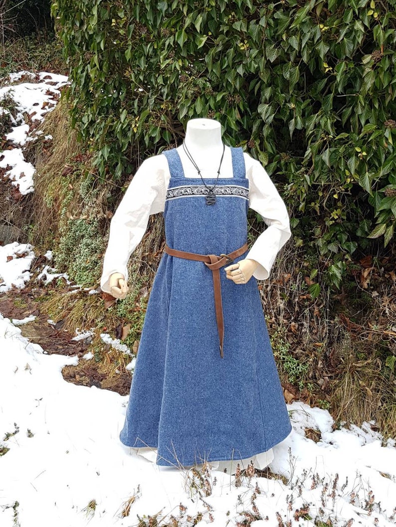 May include: A long, blue wool dress with a white linen underdress. The dress has a brown leather belt and a decorative trim around the neckline.