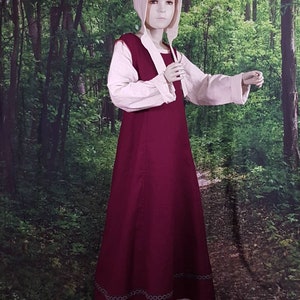 May include: A burgundy medieval style dress with a white underdress and a white linen top. The dress has a decorative trim around the hem.