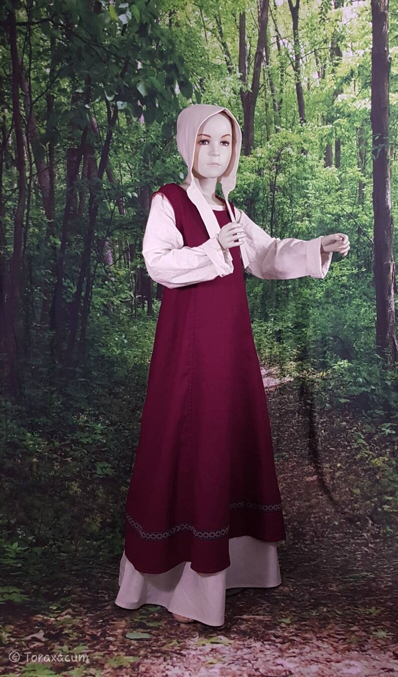 May include: A burgundy medieval style dress with a white underdress and a white linen top. The dress has a decorative trim around the hem.