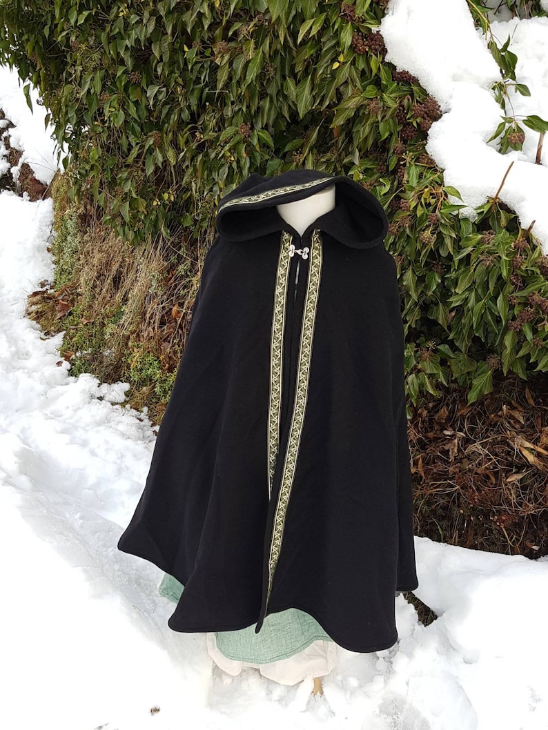 May include: A black hooded cloak with a green and gold trim. The cloak is worn over a green and white dress.
