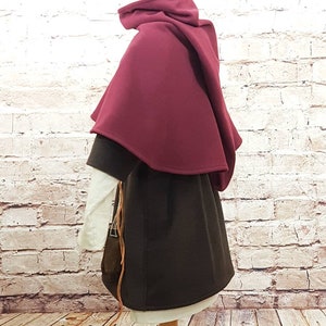May include: A burgundy hooded cloak with a brown tunic underneath. The cloak is made of a soft, warm fabric and has a simple, elegant design.