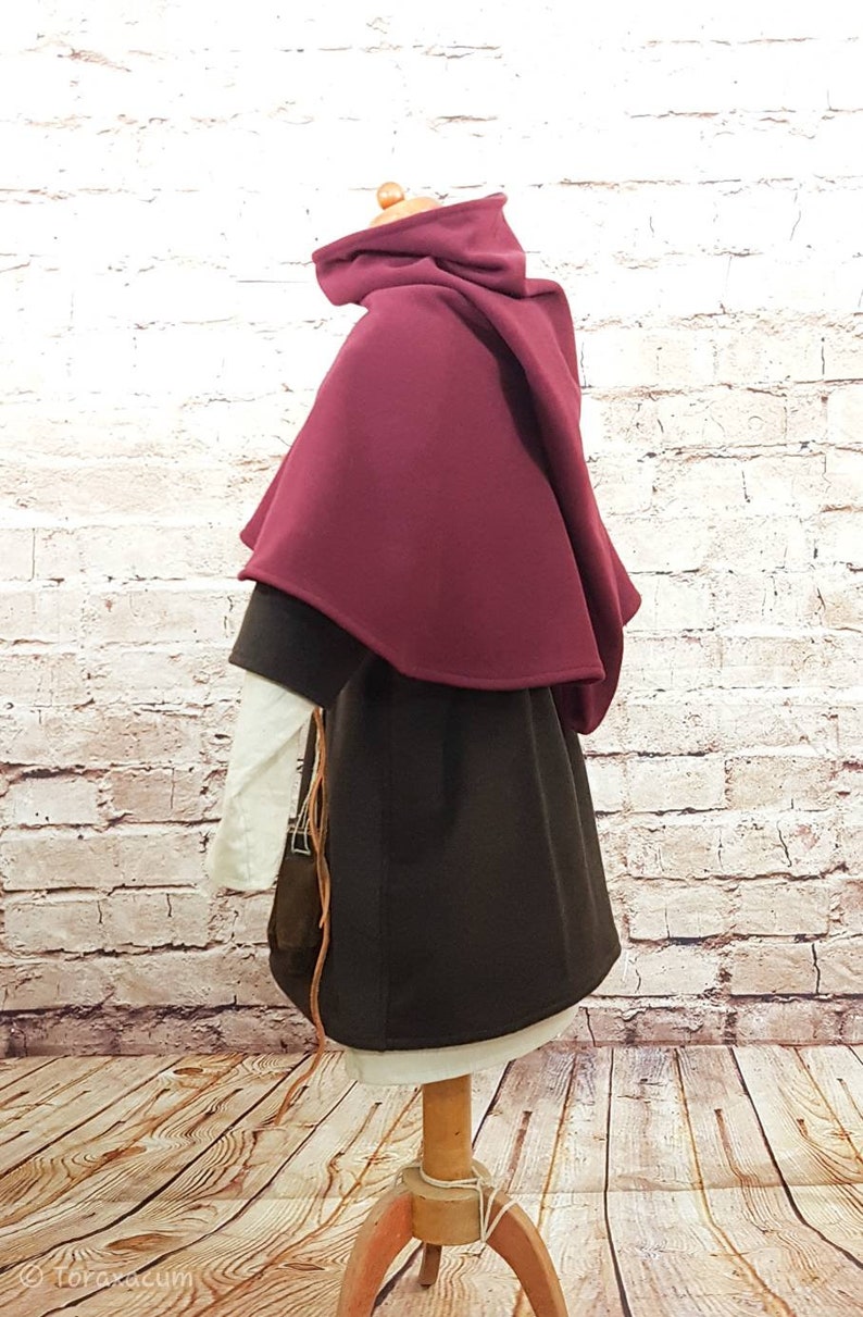 May include: A burgundy hooded cloak with a brown tunic underneath. The cloak is made of a soft, warm fabric and has a simple, elegant design.