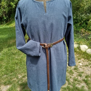 May include: A long-sleeved, blue tunic with a V-neck and a brown leather belt.