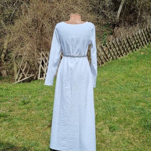 Op de afbeelding: Een witte lange mouwen jurk met een ronde hals. De jurk is getailleerd met een riem en heeft een zwierige rok.
