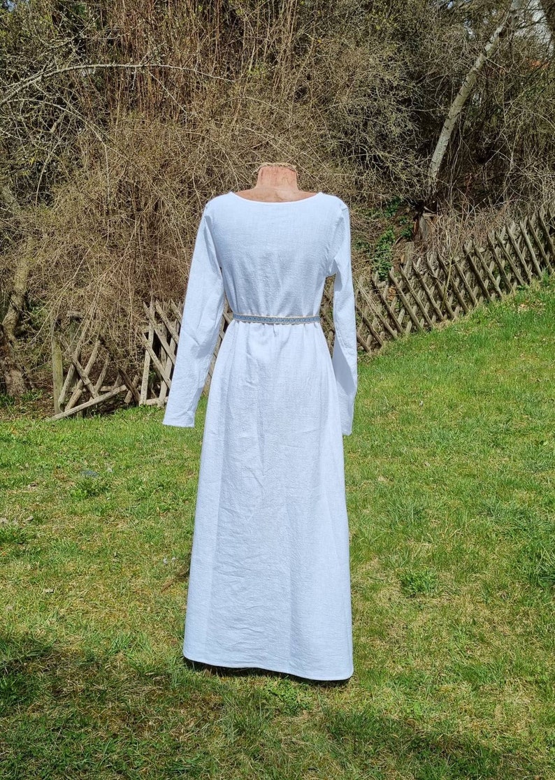 Op de afbeelding: Een witte lange mouwen jurk met een ronde hals. De jurk is getailleerd met een riem en heeft een zwierige rok.