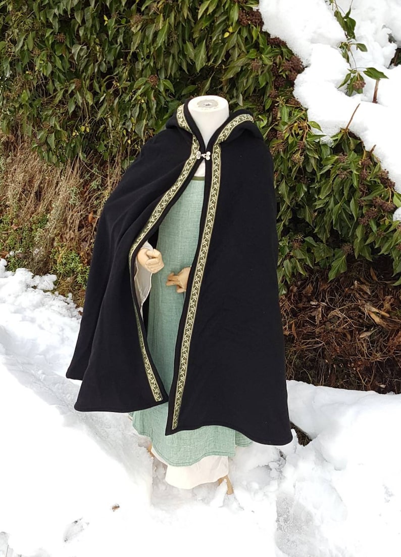 May include: Black hooded cloak with a green and gold trim. The cloak is worn over a green dress.