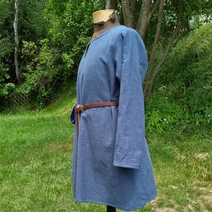 May include: A blue tunic with long sleeves and a brown leather belt. The tunic is made of a soft, textured fabric and has a simple, classic design.