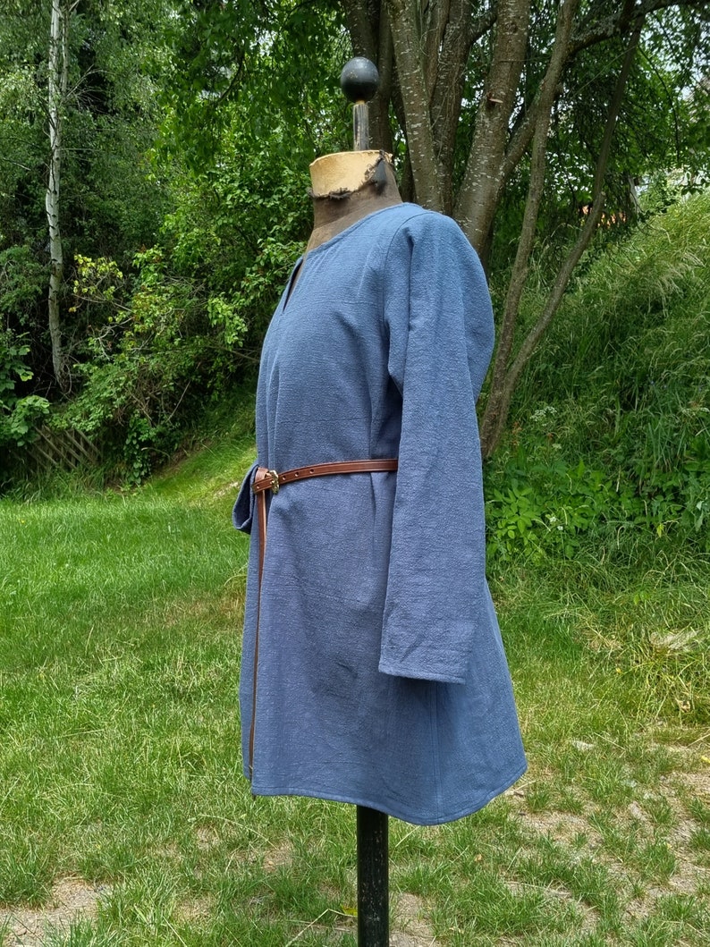 May include: A blue tunic with long sleeves and a brown leather belt. The tunic is made of a soft, textured fabric and has a simple, classic design.