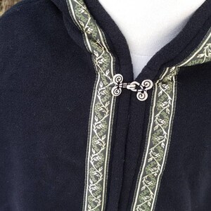 May include: Black hooded cloak with a green and gold trim. The cloak has a decorative metal clasp.