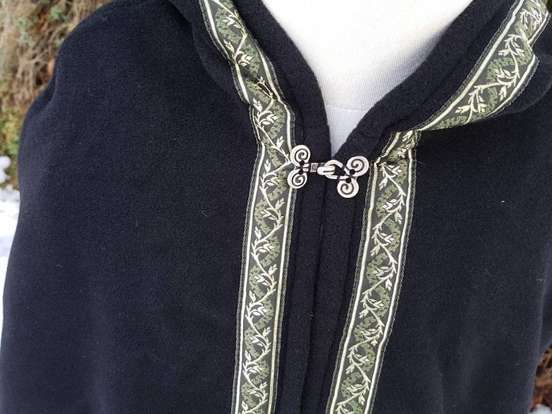May include: Black hooded cloak with a green and gold trim. The cloak has a decorative metal clasp.