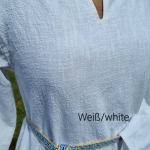 Op de afbeelding: Een witte linnen tuniek met een V-hals en lange mouwen. De tuniek is in de taille gebonden met een geweven riem in blauw en beige. De tekst "Wei&szlig;/white" is zichtbaar op de stof.