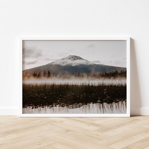 A photograph of Mt. Bachelor at sunrise with trees and fog in the foreground