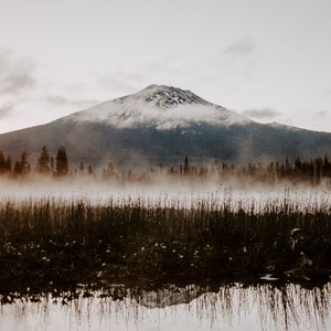 A photograph of Mt. Bachelor at sunrise with trees and fog in the foreground