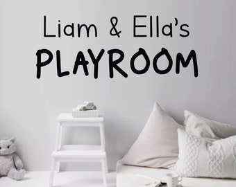 Pode incluir: Decoração de parede de sala de jogos com o texto "Liam & Ella's PLAYROOM" em preto. O quarto apresenta um banco branco com um carro de brinquedo, um urso de pelúcia e almofadas decorativas.