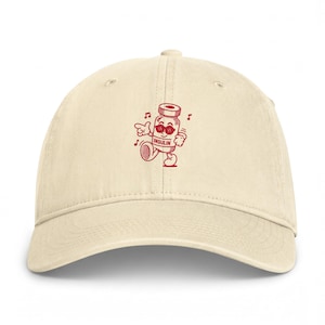May include: A cream-colored baseball cap featuring a red graphic of a cartoon insulin vial wearing sunglasses, walking, and surrounded by musical notes. The vial has the word INSULIN printed on its front. The cap has a curved brim and eyelets.