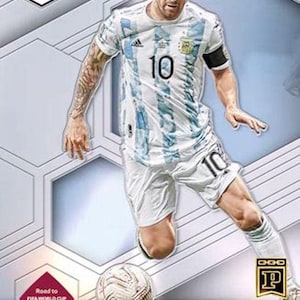 May include: A trading card featuring Lionel Messi in an Argentina soccer uniform. The card has a white and blue design with the number 10 on the jersey and shorts. The card includes the text "Road to FIFA World Cup Qatar2022".
