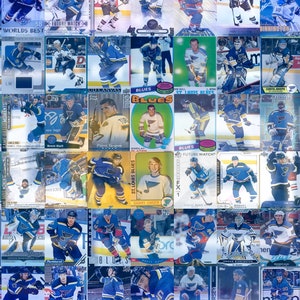 May include: A collage of trading cards featuring hockey players from the St. Louis Blues. The cards are arranged in a grid pattern and feature various players, including Brett Hull, Pierre Targeon, and Garry Unger. The cards are all in the team's colours of blue and gold.