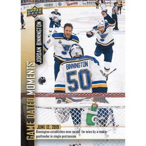 May include: A hockey card featuring a photo of Jordan Binnington, a goalie for the St. Louis Blues, celebrating a win with his teammates. The card is from the Upper Deck Game Dated Moments series and features the date 12 June 2019. The text on the card reads "Binnington establishes new record for wins by a rookie goaltender in single postseason."