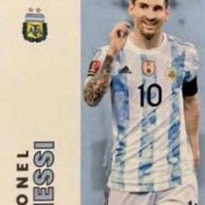 May include: A Panini trading card featuring Lionel Messi in an Argentina national team jersey. The jersey is white with light blue stripes and the number 10. The card also displays the Panini logo and the Argentina Football Association emblem.