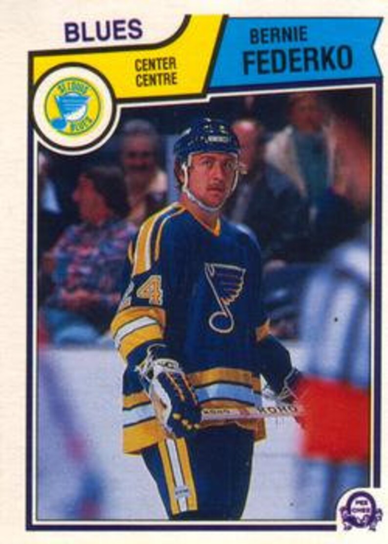 May include: A hockey player wearing a blue and yellow jersey with a blue bird logo on the front. The jersey has the number 44 on the front. The player is holding a hockey stick and is looking at the camera.